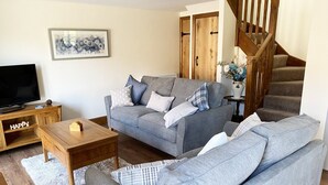 Un salon avec un canapé gris, une table basse en bois et un téléviseur posé sur un meuble en bois.