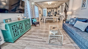 A spacious living area with a television, teal cabinet, blue sofa, and a central dining table.