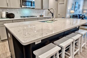 A kitchen with a large island, white bar stools, a stainless steel microwave, and a modern faucet.