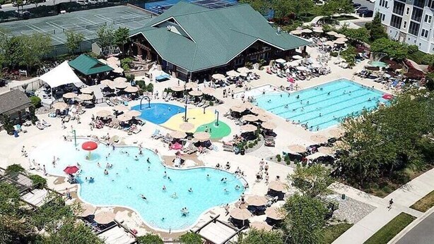 A hotel with multiple swimming pools, outdoor seating areas, and a parking lot.