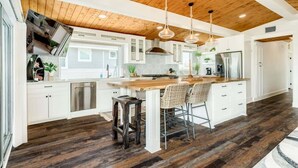 Una cocina amplia con vigas de madera en el techo, muebles blancos y una isla central con taburetes de bar.