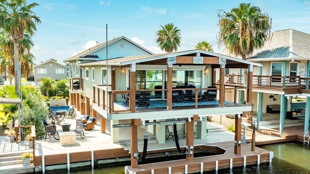 Una casa frente al agua con terraza, mobiliario exterior y piscina.
