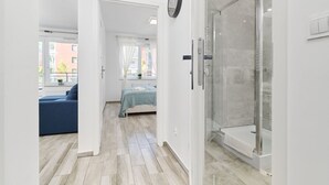 Ein modernes Schlafzimmer mit einem Bett, einem blauen Sofa, einer Duschkabine aus Glas und Blick ins Freie.