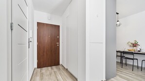 Ein Flur mit einer Holztür, weißen Wänden und einem Essbereich mit Stühlen und einem Tisch.
