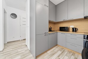 A modern kitchen with grey cabinets, a microwave, a coffee maker, and a clock on the wall. - Cozy Apartment | Balcony and Workspace (Wrocław)