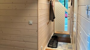 Un couloir en bois, avec une porte donnant sur une pièce lumineuse, un porte-manteau et une paire de chaussons posés sur le sol.