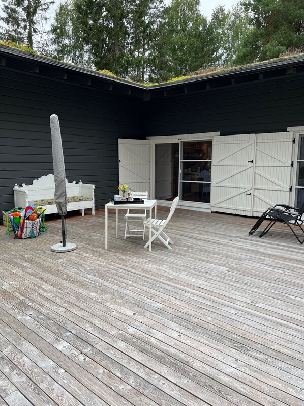Eine Holzterrasse mit einer weißen Bank, einem Tisch und einem Stuhl.