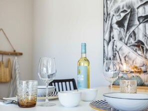 A dining table with various glassware and bowls, a bottle of white wine, and a black and white abstract painting in the background.