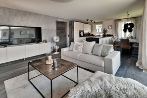 A modern living room with a sofa, coffee table, and a TV. There is a kitchen area with a dining table and chairs. - Bergcrystal (Garmisch-Partenkirchen)