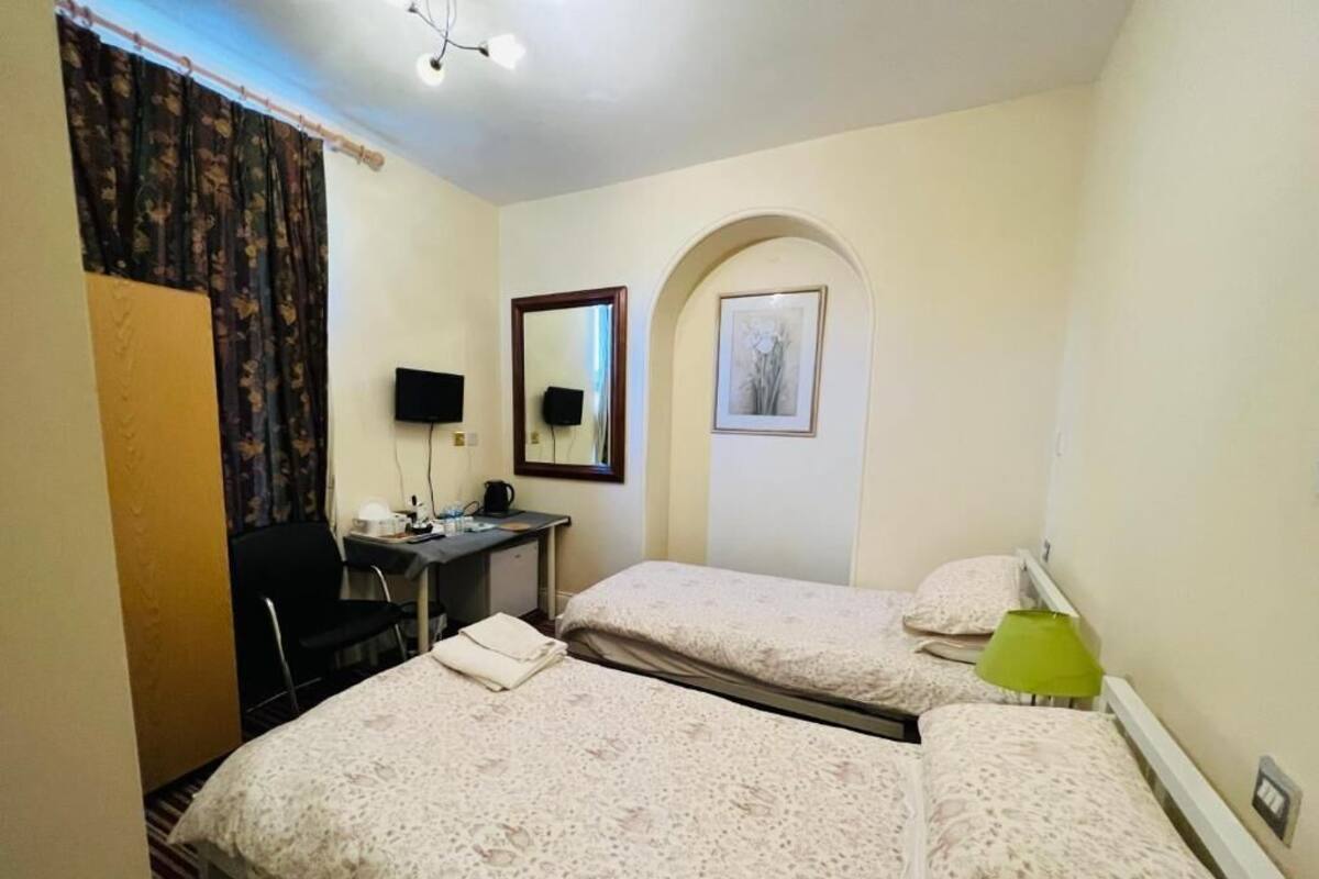 A hotel room with two beds, a desk with a chair, a flat-screen TV, and a small table with a lamp.