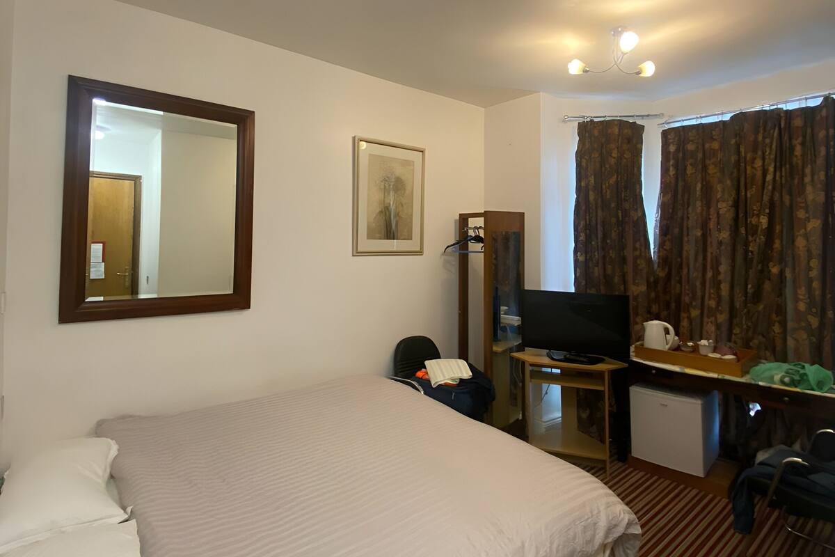 A hotel room with a large bed, a desk with a computer, a television, and a small refrigerator.