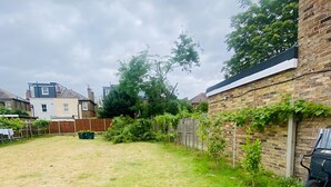 A residential backyard with a grassy lawn, a brick wall with climbing plants, and a wooden fence. - Second Home (London)