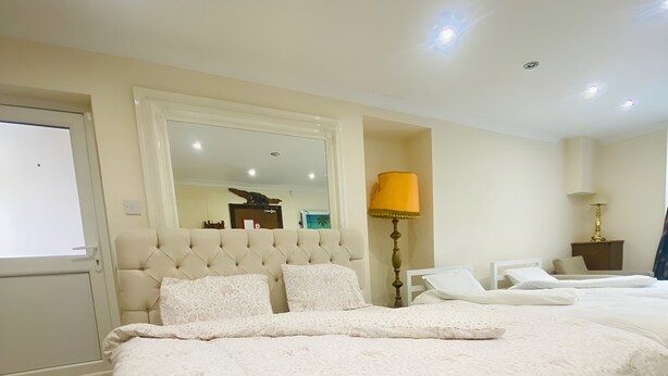 A hotel room with a large bed, a bedside table with a lamp, a mirror, and a door with a view of the outside. - Second Home (London)