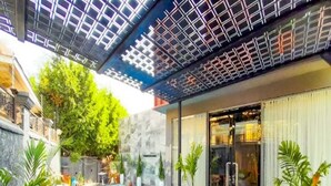 Un área de piscina exterior moderna con acceso por puerta de vidrio, rodeada de plantas en macetas y mobiliario de exterior.