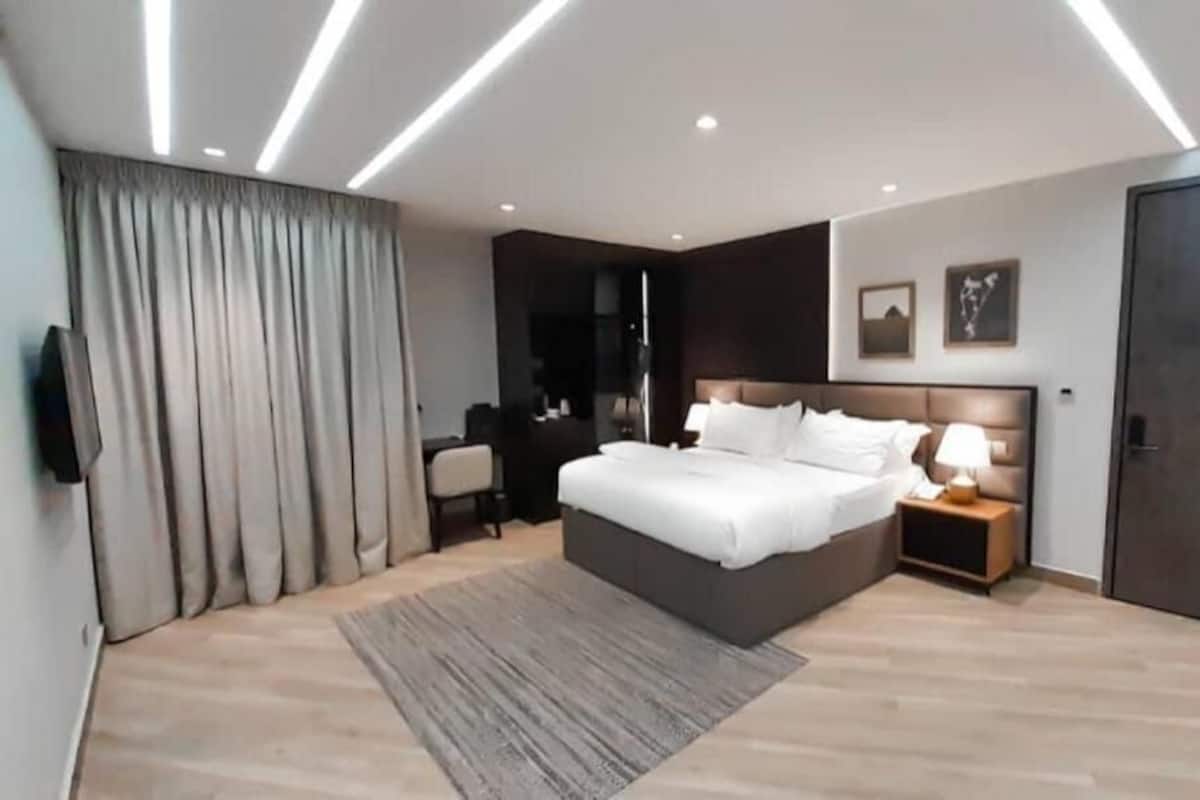 A modern bedroom with a large bed, bedside tables, a TV, and a wardrobe.