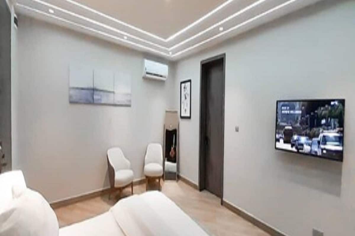 A modern bedroom with a bed, two chairs, a TV, and artwork on the wall.