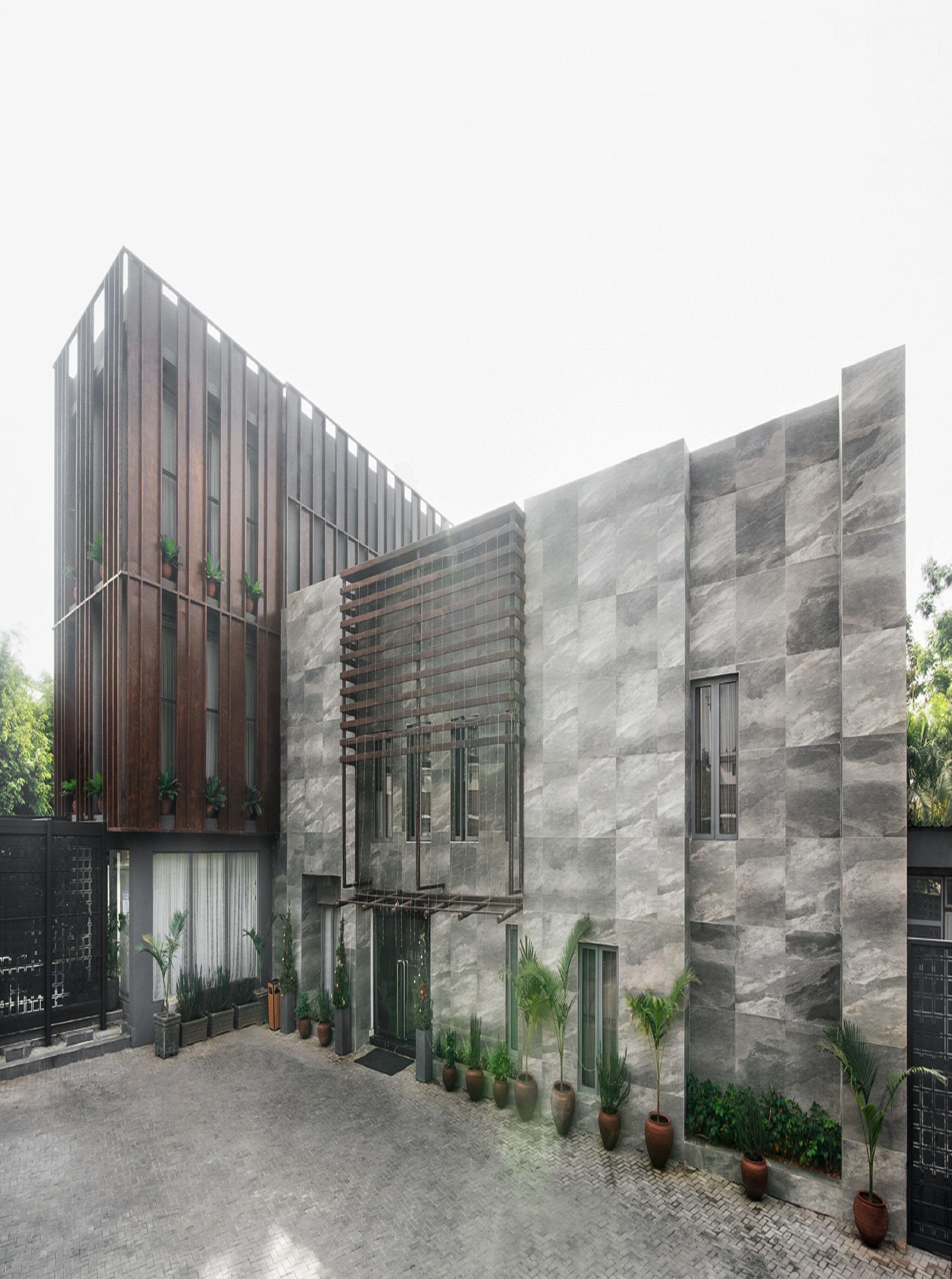 A modern building with a courtyard, featuring a mix of wooden and stone facades, and potted plants along the perimeter.