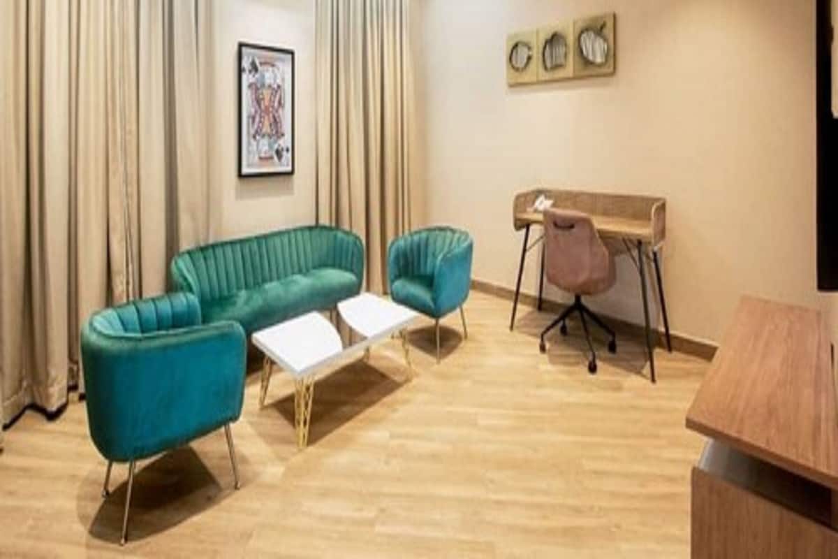 A modern room with a green sofa, a small table, a desk with a chair, and a painting on the wall.