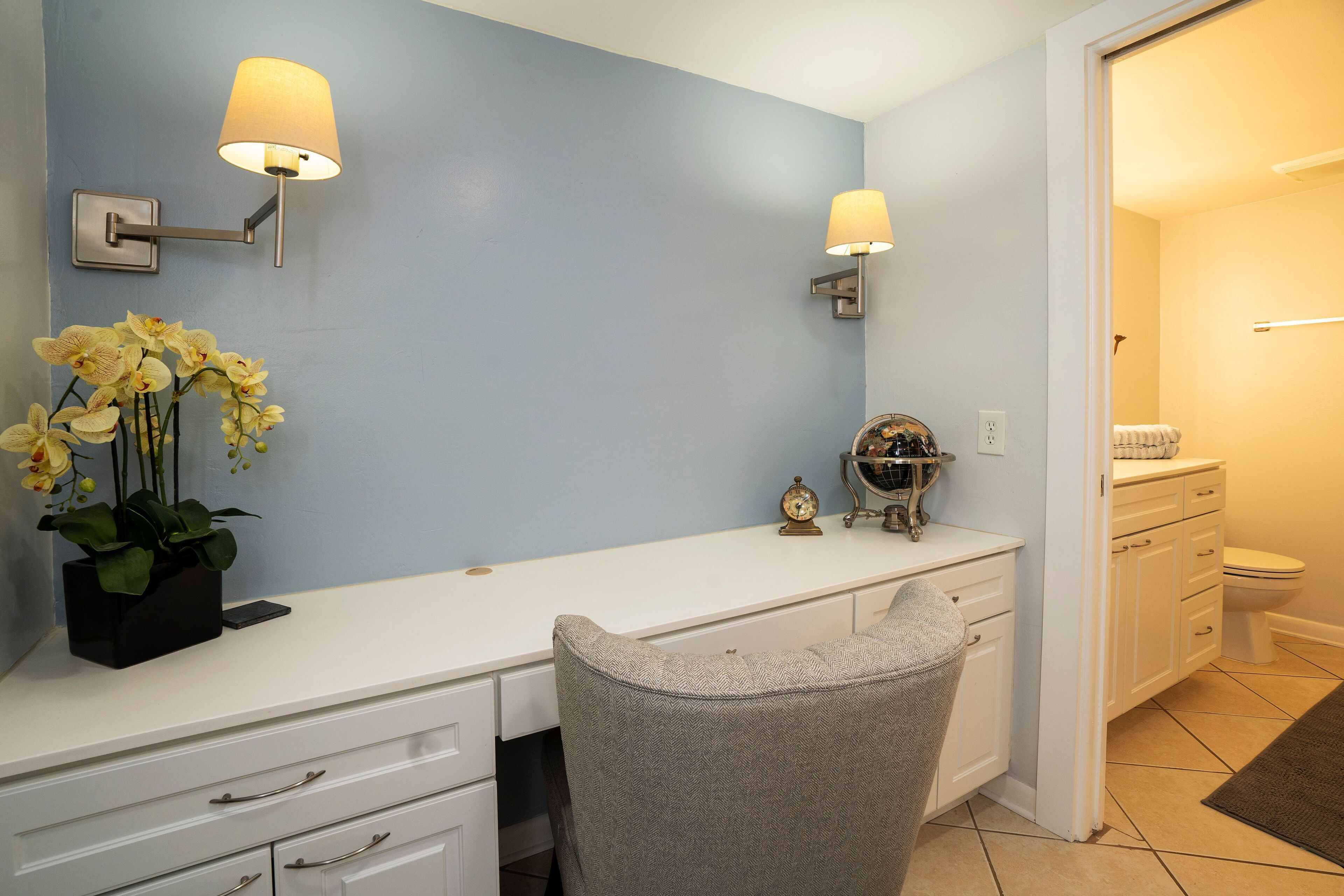 A bathroom with a white vanity, two wall-mounted lamps, a toilet, and a small plant.