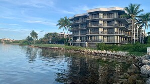 A multi-story hotel with balconies, located near a body of water with palm trees and a rocky shoreline. - 1800 Atlantic Condo in Key West – Stylish 2BR with Pool, Tennis & Beach (Key West)