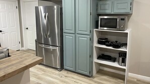 A kitchen with a stainless steel refrigerator, a microwave, and a shelf with cookware.
