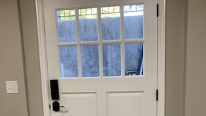 A white door with a window above it, a small rug in front, and a light switch on the wall to the left.