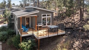 Une maison moderne dotée d’une terrasse, d’un barbecue extérieur et offrant une vue sur une zone boisée.