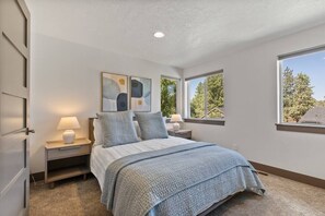 A bedroom with a bed, two bedside tables with lamps, a window, and abstract wall art.