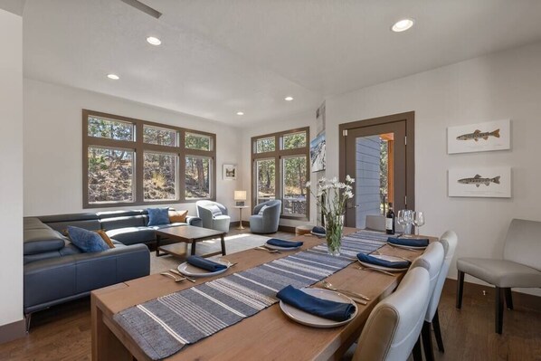 A modern dining area with a long wooden table set for six, flanked by blue sofas and a seating area with a sofa and chairs.