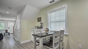 Uma área de refeições com mesa e cadeiras, uma janela com persianas e uma cozinha ao fundo.