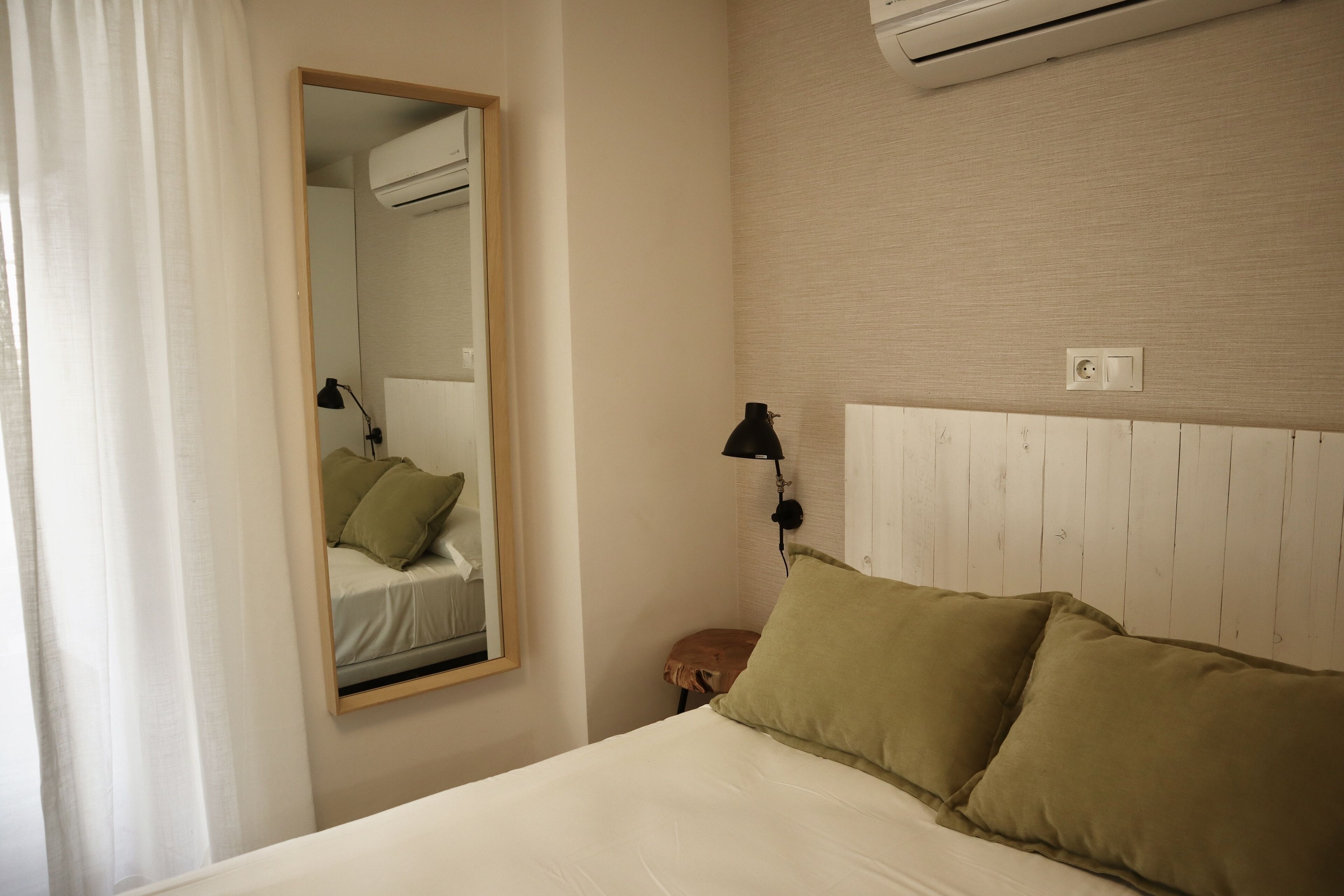 Ein Hotelzimmer mit Bett, Spiegel, Wandklimaanlage, Nachttischlampe und Steckdose.