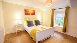 Quarto com cama, mesas de cabeceira, janela com cortinas e um quadro na parede.