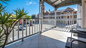A balcony with a view of a street and buildings, a tiled floor, and a metal railing.