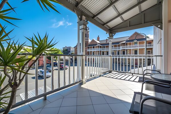 A balcony with a view of a street and buildings, a tiled floor, and a metal railing.