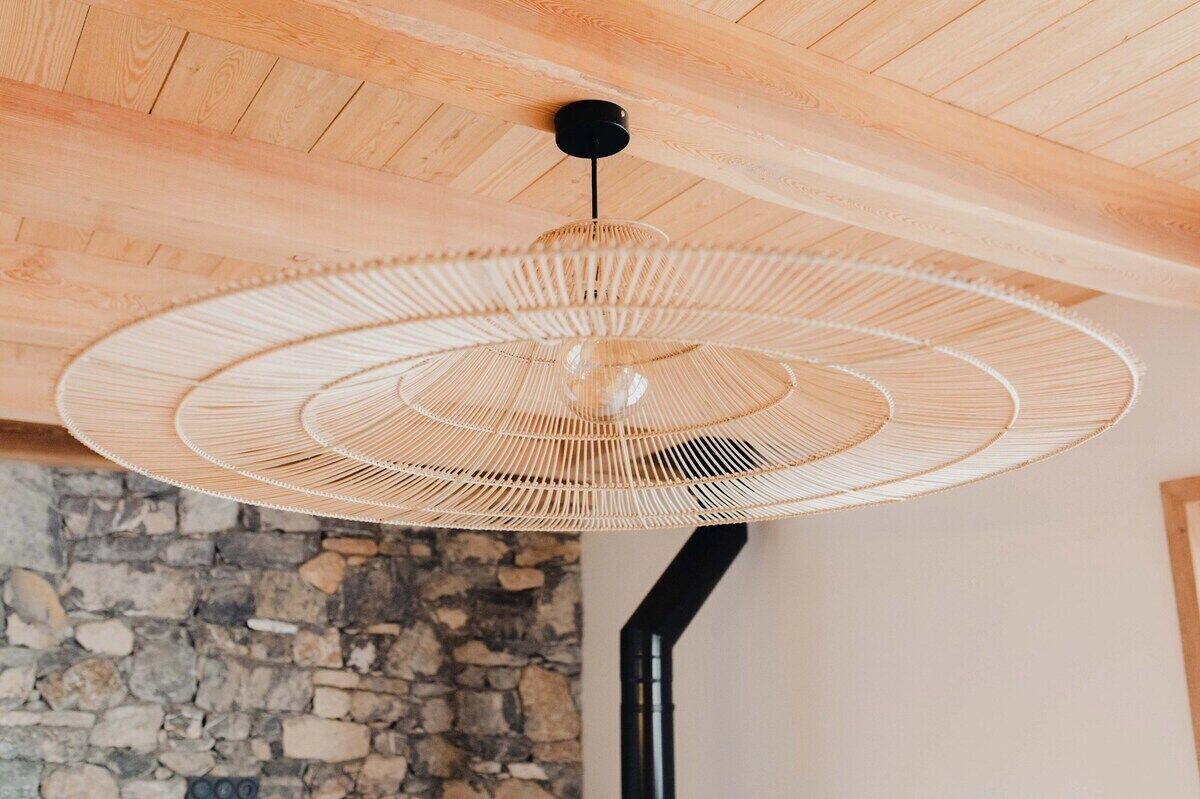 A ceiling with a woven light fixture and a stone wall.