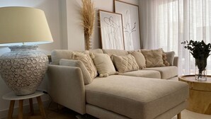 Een moderne woonkamer met een beige bank, een grote, gestructureerde vaas en een klein houten bijzettafeltje.