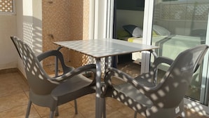 Een balkon met een tafel en stoelen, een betegelde muur en een schuifdeur die leidt naar een slaapkamer.
