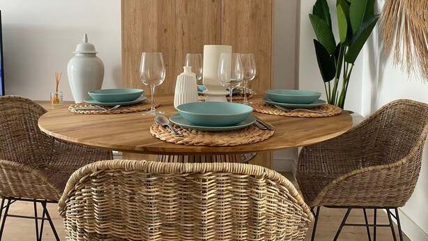 Een ronde houten eettafel met blauwgroene borden, witte kaarsen en glazen wijnglazen.