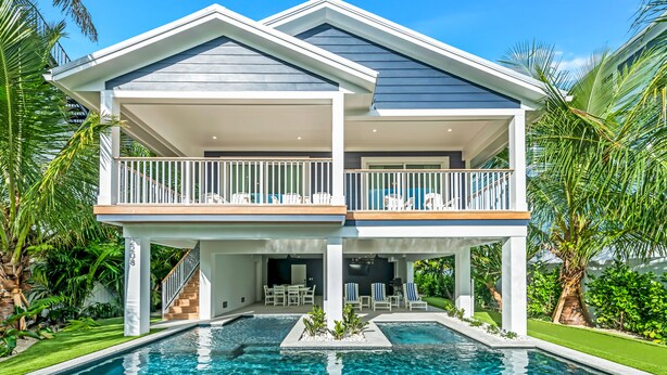 Ein modernes, zweistöckiges Haus mit Pool, überdachten Balkonen und üppiger Bepflanzung.