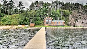 Een houten huis met een terras dat uitsteekt over het water, omringd door een dicht bos.