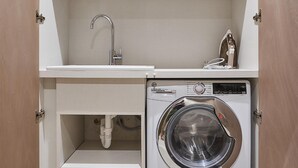 Un área de lavandería compacta con lavadora, un lavabo y un estante pequeño.