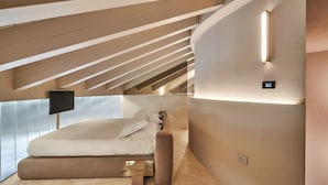 Ein modernes Schlafzimmer mit schrägem Dach, einem Bett, einem Nachttisch und einem an der Wand befestigten Fernseher.
