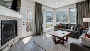 Een moderne woonkamer met een open haard, een zithoek, een salontafel en grote ramen met uitzicht op de omgeving.