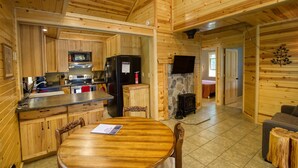 Ein Holzblockhaus im Inneren mit Küche, Essbereich und Kamin aus Stein.