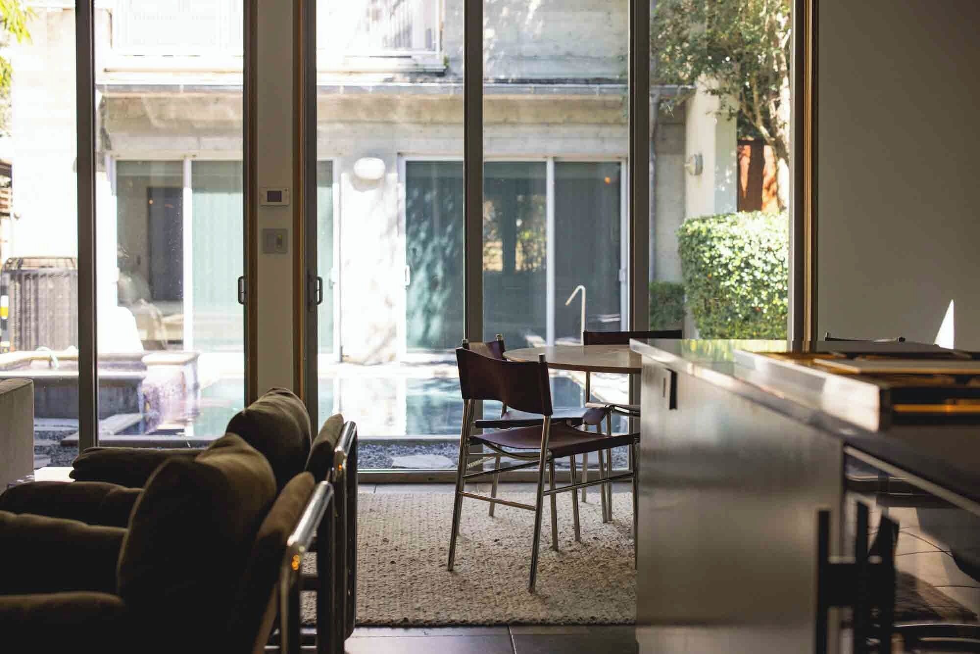 Une pièce comprenant un canapé, une table et des chaises, située près de grandes fenêtres offrant une vue sur un bâtiment et la verdure environnante.