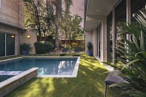 A swimming pool with a surrounding lawn, a wooden deck, and potted plants.