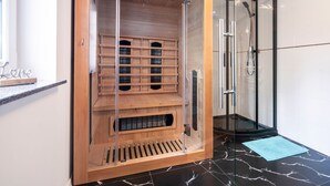 Una sauna amb interior de fusta, portes de vidre i un paviment de rajoles negres.