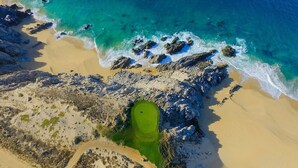 Eine Luftaufnahme einer Küstenlandschaft mit Sandstrand, felsiger Küste und einem grünen Golfplatz.