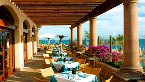 Ein Essbereich im Freien mit Tischen und Stühlen, einer Holzpergola und Meerblick.