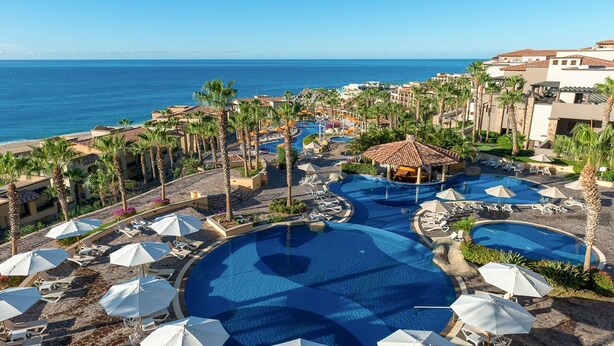 Ein Resort mit mehreren Swimmingpools, Palmen und Blick auf den Ozean.